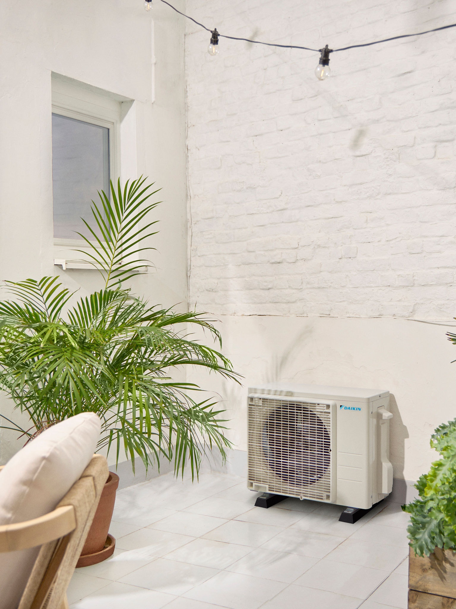 Εξωτερική μονάδα της Daikin σε λευκή βεράντα με ένα φυτό
