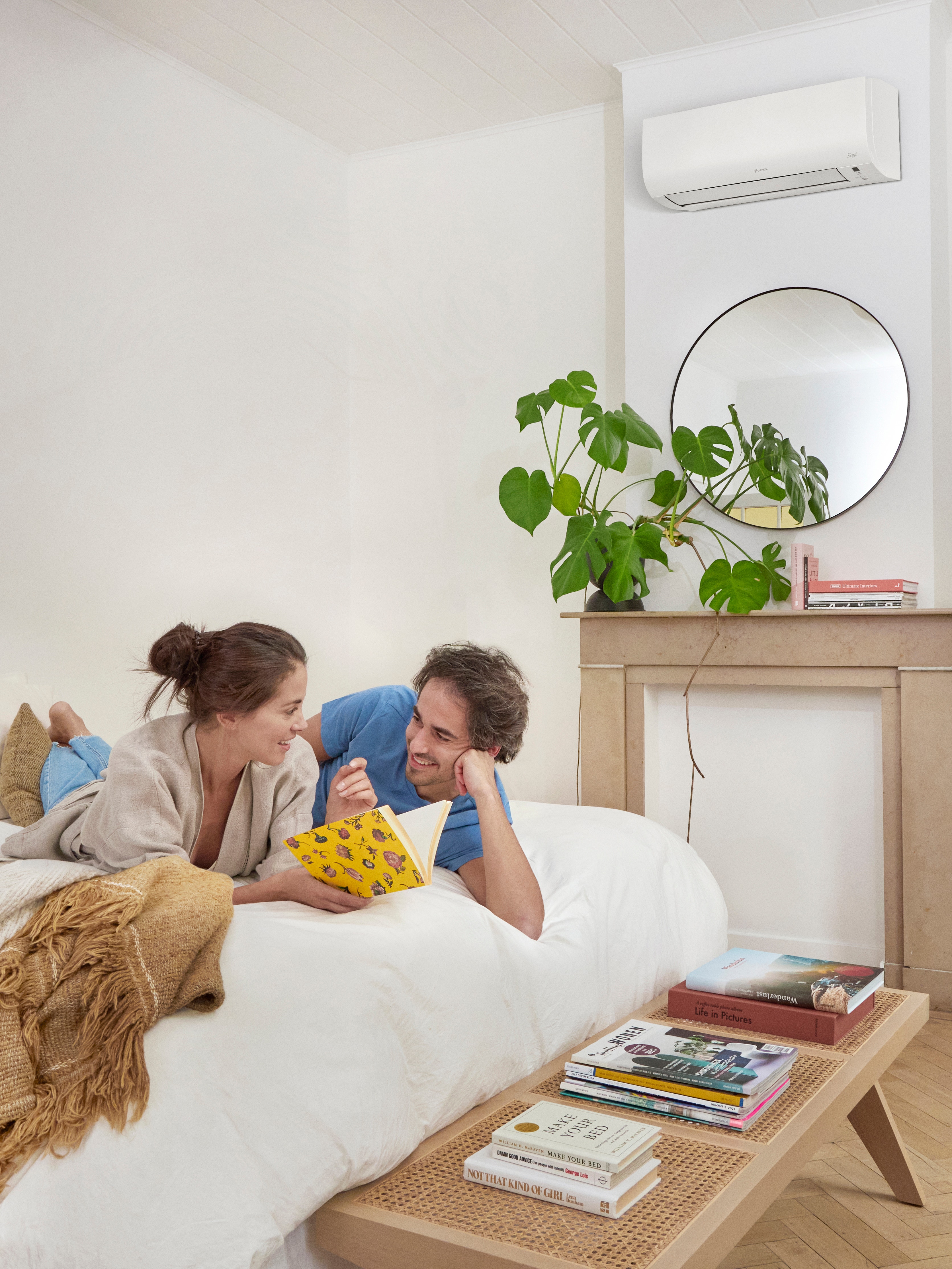 Par, der ligger på deres seng i soveværelset og smiler til hinanden, mens kvinden holder en bog