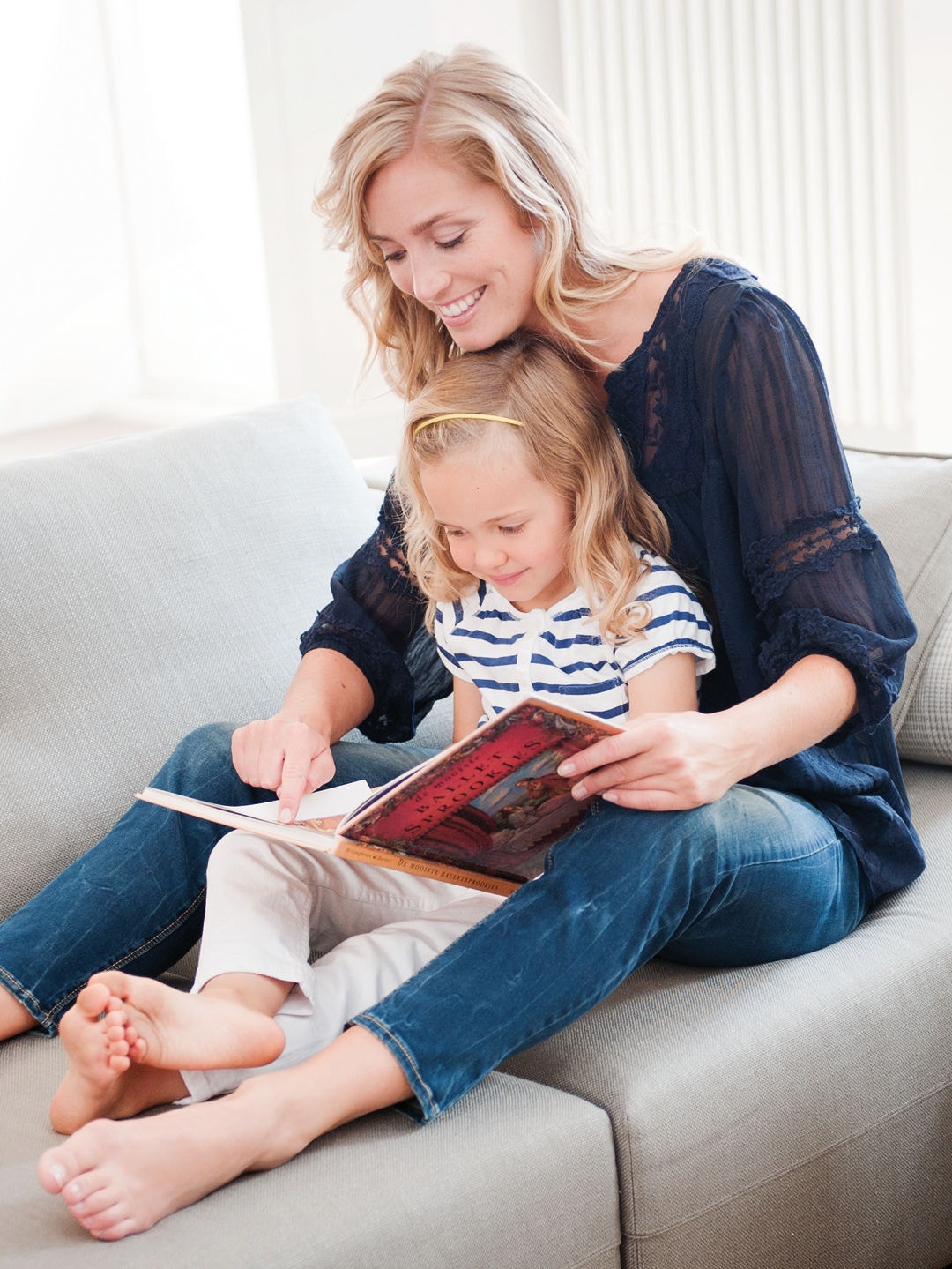 Mor i sofa med lille datter på skødet, der kigger i en bog sammen.