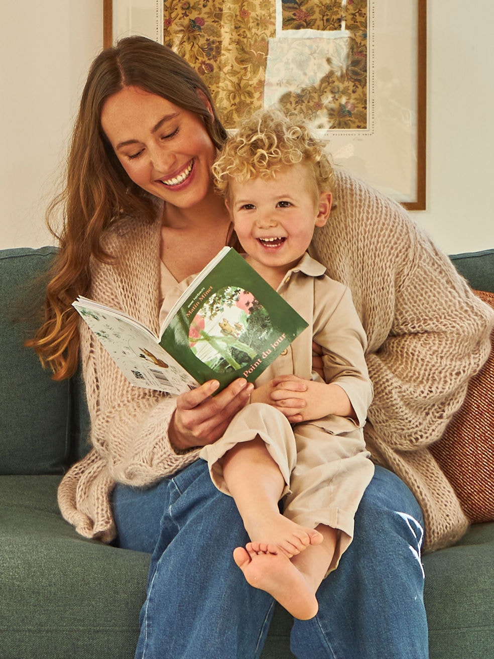En mor sidder med sit barn på skødet og kigger i en lille bog.
